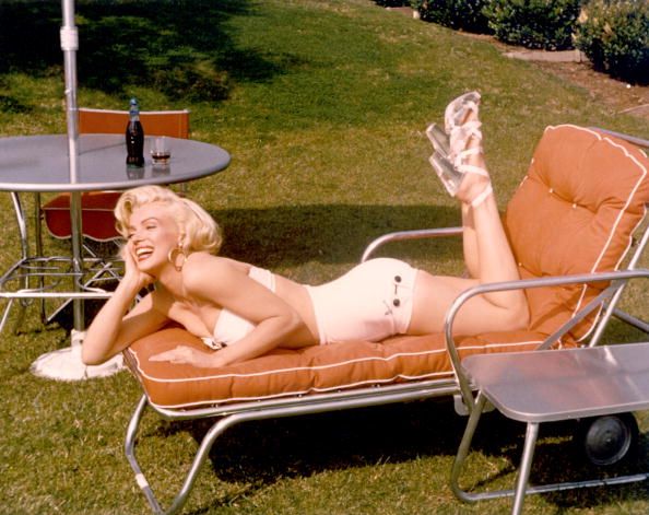 Actress Marilyn Monroe poses for a portrait in a bathing suit and high heels with a bottle of Coca-Cola in a glass on a table behind her | Photo: Getty Images