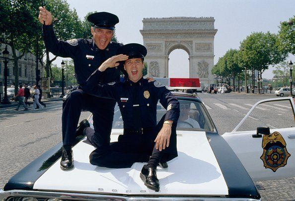 G.W. Bailey and Lance Kinsey ride on a police car down the Champs-Elysees | Photo: Getty Images